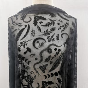Könnte beinhalten: Schwarzer, durchsichtiger Stoff mit einem sich wiederholenden Muster aus himmlischen und botanischen Elementen. Das Design umfasst Monde, Schlangen, Farne, Pilze und andere okkulte Symbole. Der Stoff ist drapiert und zeigt die feinen Details des Drucks.