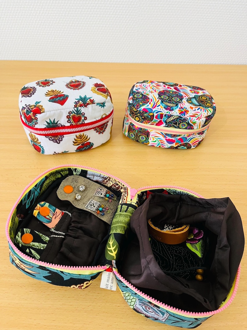 May include: Two small, rectangular zipped pouches with colourful prints: one featuring red sacred hearts on white, the other with multi-coloured sugar skulls. An open pouch displays a black interior with a small organiser flap and a drawstring compartment.
