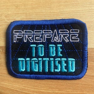 May include: A black and blue embroidered patch with the text "PREPARE TO BE DIGITIZED" in white and teal lettering.