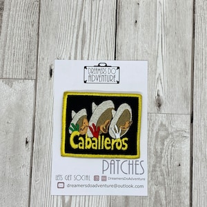 May include: A black and yellow embroidered patch featuring three cartoon figures wearing sombreros and the text "Caballeros". The patch is on a white background with the text "Dreamers Do Adventure" above it.