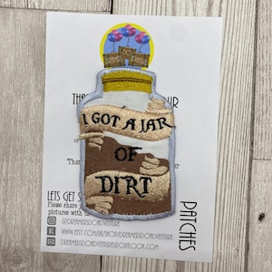 May include: A brown and white embroidered iron-on patch with a jar of dirt and the text "I got a jar of dirt".