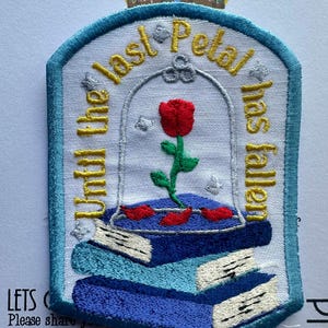 May include: Embroidered patch featuring a red rose under a glass dome, atop a stack of blue books. Text reads "Until the last petal has fallen." The patch has a light blue border and is likely for clothing or accessories.