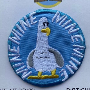 May include: A blue and white embroidered patch featuring a cartoon seagull with the text "Mine Mine Mine" around the edge.