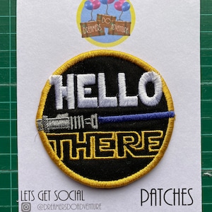 May include: A black and gold embroidered patch with the text "HELLO THERE" in white and blue. The patch features a lightsaber graphic.