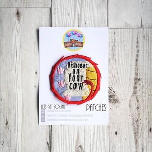 May include: A red, white, and yellow embroidered patch with the text "Dishonor on your cow" in white. The patch is on a white card with the text "Dreamers Do Adventure" and "Patches" in black.