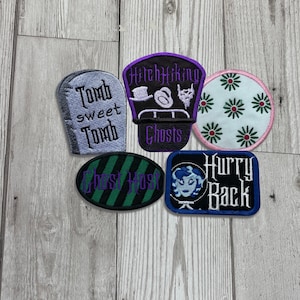 May include: Five embroidered iron-on patches with a Halloween theme. The patches feature a tombstone with the text "Tomb sweet Tomb", a hitchhiking ghosts patch with the text "Hitchhiking Ghosts", a floral patch with green flowers on a white background, a green and black striped patch with the text "Ghost Host", and a blue patch with a ghost and the text "Hurry Back".