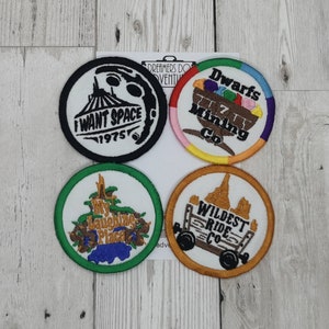 May include: Four embroidered patches with different designs. The first patch is black and white with a space mountain design and the text "I Want Space 1975". The second patch is multi-colored with a mining cart and the text "Dwarfs Mining Co.". The third patch is green with a tree and the text "My Laughing Place". The fourth patch is orange with a mine cart and the text "Wildest Ride Co."