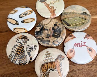 May include: Seven circular pinback buttons featuring diverse designs including a football stadium, a tiger, makeup supplies, ballet flats with Mizzou text, a tiger with a champagne tower, and hands holding lipsticks with the text miz and go tigers!