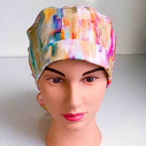 May include: A colorful surgical scrub hat with an abstract watercolor pattern in shades of pink, yellow, blue, and green.
