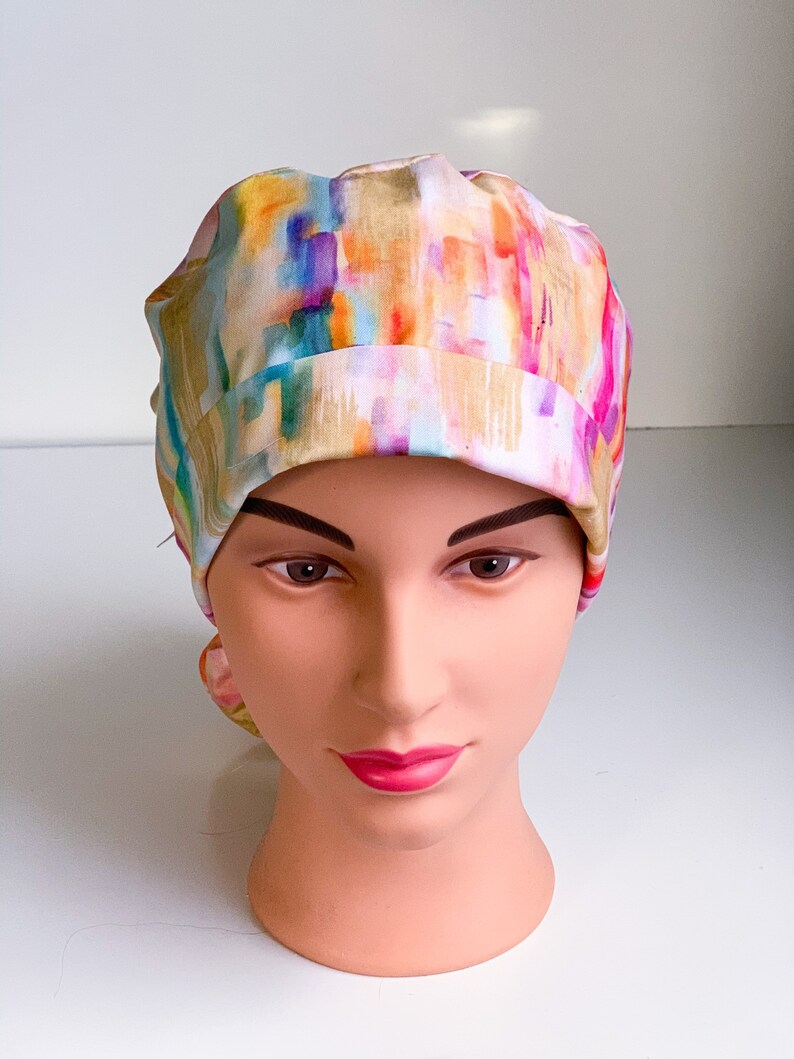 May include: A colorful surgical scrub hat with an abstract watercolor pattern in shades of pink, yellow, blue, and green.