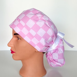 May include: Pink and white checkered surgical scrub hat with a white tie. The hat has a ponytail hole in the back.