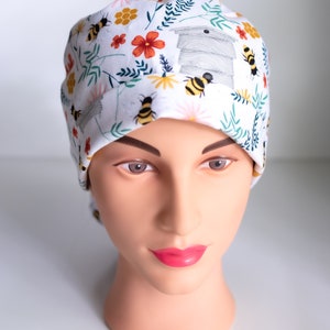 May include: A white scrub hat with a floral pattern featuring bees, flowers, and a honeycomb design.