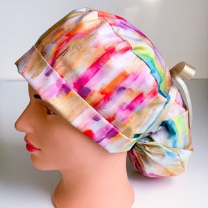 May include: A colorful surgical scrub hat with a watercolor-like pattern of pink, orange, yellow, and blue stripes. The hat has a tie at the back.
