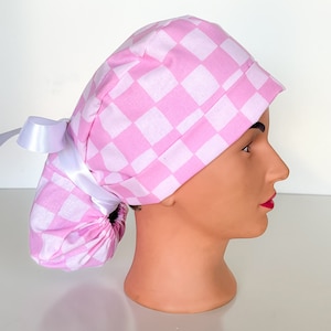 May include: Pink and white checkered surgical scrub hat with a white satin tie. The hat is designed to be worn with a ponytail.