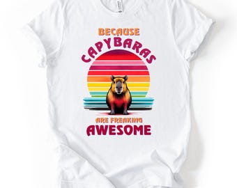 May include: White t-shirt featuring a colorful graphic of a capybara in front of a sunset. The text reads "BECAUSE CAPYBARAS ARE FREAKING AWESOME" in a playful font. A fun and unique design for animal lovers.