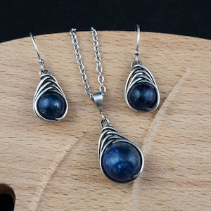 Pode incluir: Um conjunto de brincos de prata e um colar com uma pedra preciosa azul escura em um design de gaiola de arame.