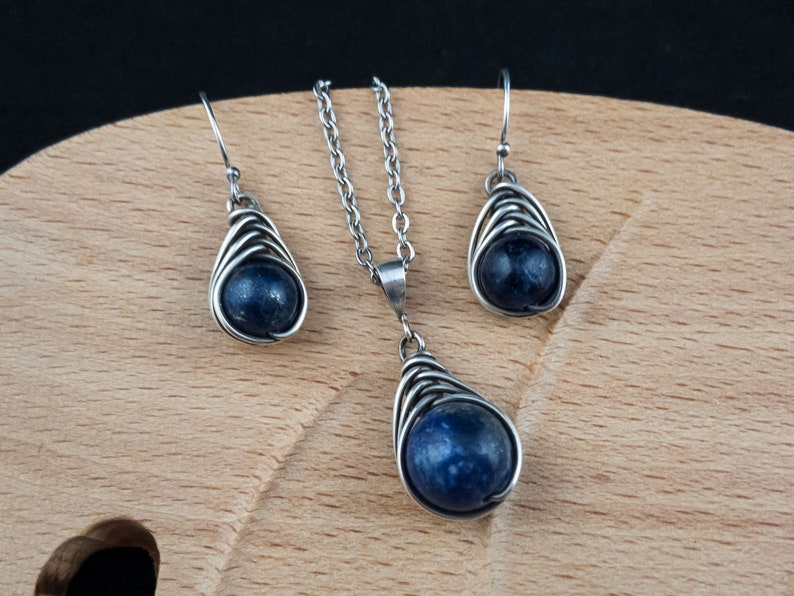 Pode incluir: Um conjunto de brincos de prata e um colar com uma pedra preciosa azul escura em um design de gaiola de arame.