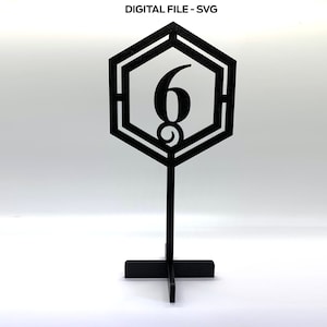 May include: Black table number six with a geometric hexagonal design. The number is centred in the hexagon and the stand is a simple cross shape.