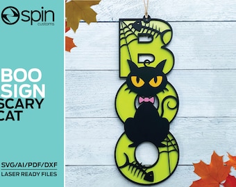 May include: A green and black Halloween sign with the word "BOO" in large letters. The "O" is a circle with a black cat sitting inside. The cat has a pink bow tie and yellow eyes. The letters are decorated with spiderwebs and bones.