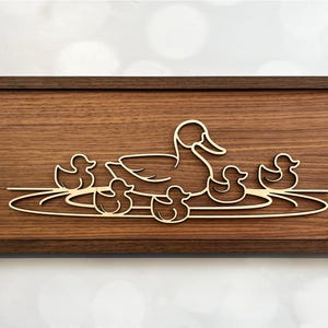 May include: A wooden wall art piece with a cutout design of a mother duck and her ducklings swimming in a pond. The design is in a light brown color against a dark brown wood background.
