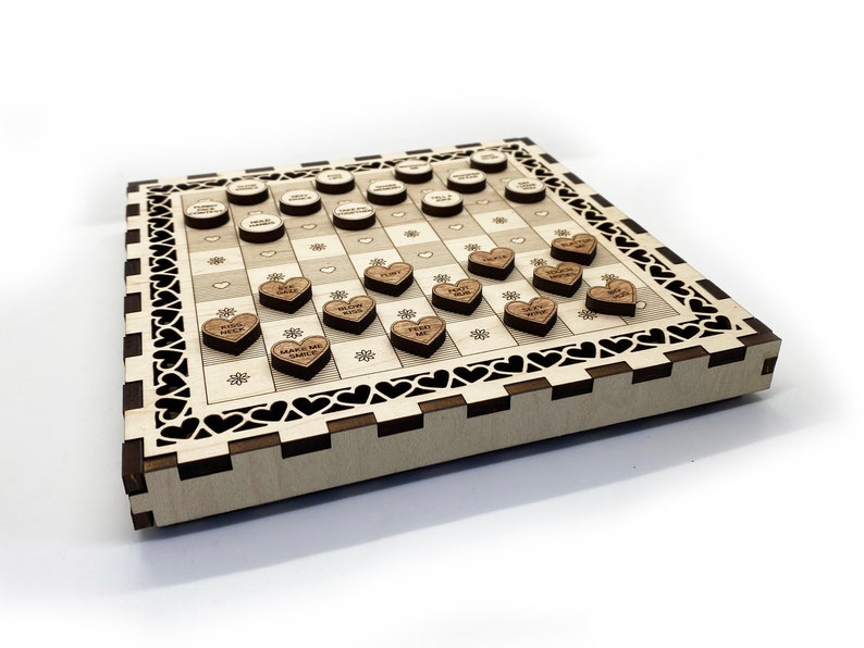 May include: A wooden game board with a checkerboard pattern and a heart-shaped border. The board is decorated with small wooden hearts, each with a different message on it. The messages include "Make Me Smile", "Kiss Me", "Hug Me", and "I Love You".