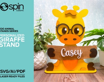 Könnte beinhalten: Ein gelber Giraffenständer mit personalisiertem Namensschild. Die Giraffe hat braun umrandete Brillen und eine braune und orangefarbene Nase. Der Ständer gehört zur Zoo Animal Stands Serie und ist laserfertig.