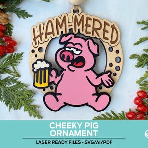 May include: A wooden ornament featuring a cartoon pig holding a beer mug. The pig is pink with black outlines and the text "HAM-MERED" is above it. The ornament is surrounded by a horseshoe shape with circular cutouts. The words "CHEEKY PIG ORNAMENT" are at the bottom.