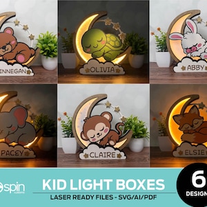 May include: A collection of six crescent moon-shaped wooden light boxes featuring sleeping animals including a bear, turtle, rabbit, elephant, monkey, and fox. Each lamp displays a name: Finnegan, Olivia, Abby, Pacey, Claire, and Elsie. The text KID LIGHT BOXES and 6 DESIGNS is visible at the bottom.