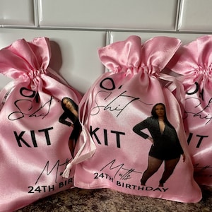 May include: Four pink satin drawstring bags with a black and white design. Each bag features a woman in a black outfit, the text "O' Shit Kit" and the number "24th Birthday".