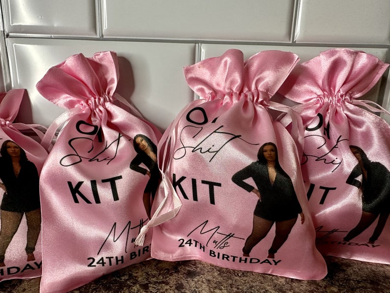 May include: Four pink satin drawstring bags with a black and white design. Each bag features a woman in a black outfit, the text "O' Shit Kit" and the number "24th Birthday".