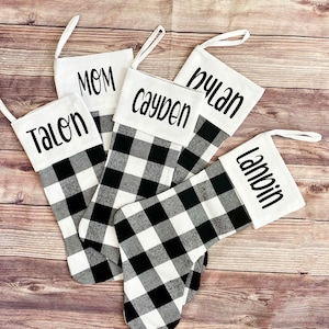 May include: Five black and white buffalo plaid Christmas stockings with white fabric cuffs. The cuffs are personalized with the names "Talon", "Mom", "Cayden", "Dylan", and "Landin".