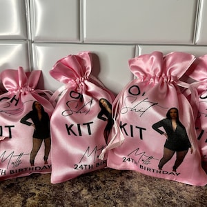 May include: Five pink satin drawstring bags with the text "O' Shit Kit" and a woman in a black outfit printed on them. The bags also have the text "Matt's 24th Birthday" printed on them.