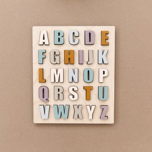 May include: A wooden alphabet puzzle with letters A through Z in various pastel colors, including light blue, light purple, light pink, and orange.