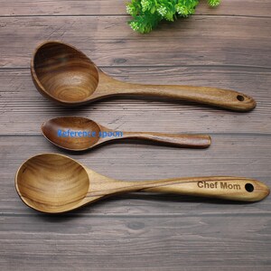 Op de afbeelding: Drie houten lepels op een houten oppervlak. De grootste lepel is een soeplepel met een ronde kom. De middelste lepel is kleiner en heeft een ronde kom. De kleinste lepel is een serveerlepel met een ronde kom. De grootste lepel heeft de tekst "Chef Mom" gegraveerd op het handvat.