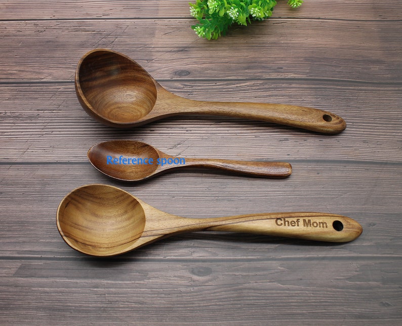 Op de afbeelding: Drie houten lepels op een houten oppervlak. De grootste lepel is een soeplepel met een ronde kom. De middelste lepel is kleiner en heeft een ronde kom. De kleinste lepel is een serveerlepel met een ronde kom. De grootste lepel heeft de tekst "Chef Mom" gegraveerd op het handvat.