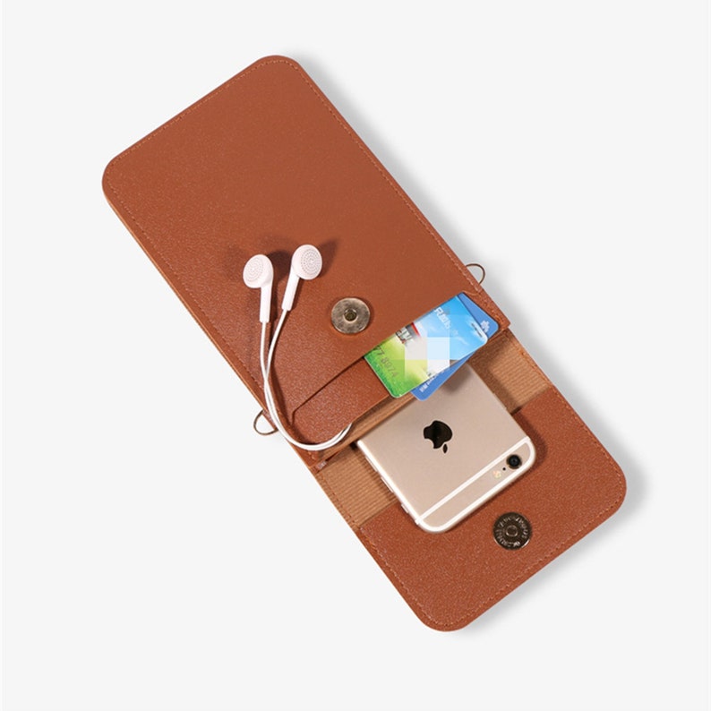 May include: A brown leather phone case with a flap that closes with a snap. The case has a pocket for a credit card and a slot for headphones. A gold smartphone is inside the case.
