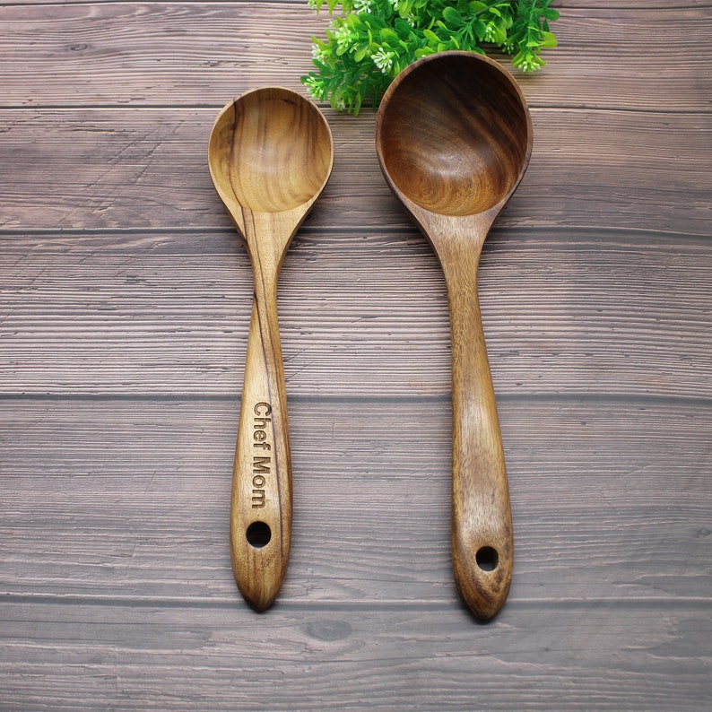 Op de afbeelding: Twee houten lepels, een met een grotere kom en de andere met een kleinere kom. De grotere lepel heeft een handvat met de woorden "Chef Mom" erop gegraveerd.