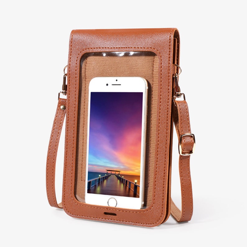 May include: A brown faux leather crossbody phone bag with a clear plastic window to display a smartphone. The bag has a gold-toned buckle and adjustable strap.
