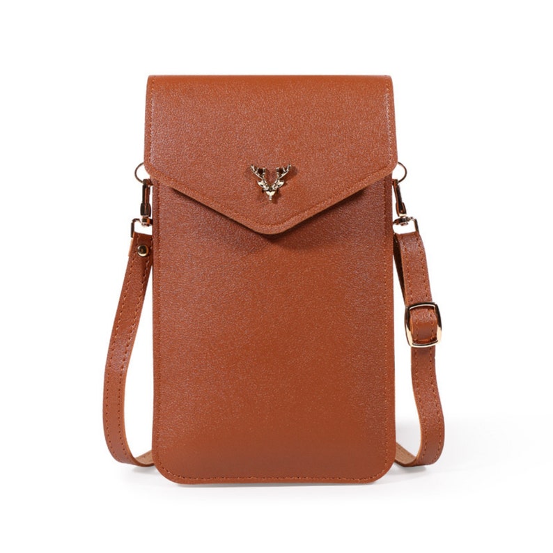 May include: A brown leather crossbody phone bag with a gold deer head accent. The bag has a flap closure and a long adjustable strap.