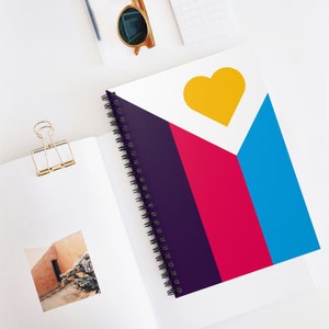 May include: A spiral bound notebook with a colourful geometric design. The cover features a large yellow heart shape at the top, followed by a purple, pink, and blue stripe pattern.
