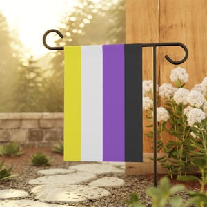 Peut inclure: Un drapeau de jardin rectangulaire composé de quatre bandes verticales jaune, blanche, violette et noire. Le drapeau est suspendu à un support en métal noir, affichant les couleurs de la fierté non-binaire dans une orientation verticale.