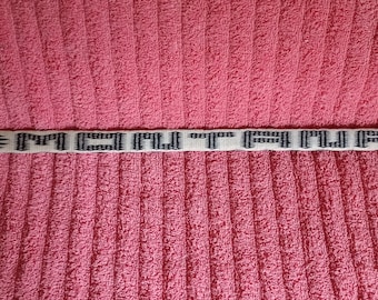 May include: A white woven belt with black lettering that reads "MONTURA" and black flame-like designs on either end.