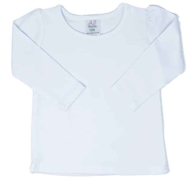 Puede incluir: Camiseta blanca de manga larga con cuello redondo. La camiseta tiene una peque&ntilde;a etiqueta con el texto "AJ Brands 12M" en la parte delantera.
