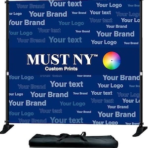 May include: A blue backdrop with the text "MUST NY" and "Custom Prints" in white. The backdrop is covered in a repeating pattern of the text "Your Brand", "Your Logo", and "Your Text" in white. A color wheel is visible in the upper right corner of the backdrop. The backdrop is attached to a black stand with a black carrying case in the foreground.