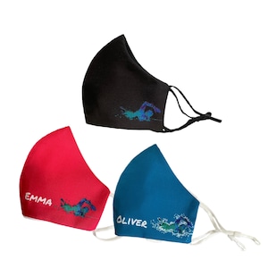 May include: Three face masks in black, red, and blue. Each mask features a swimmer graphic in shades of blue and green. The red mask has the name "EMMA" in white, and the blue mask has "OLIVER". All masks have adjustable ear loops.