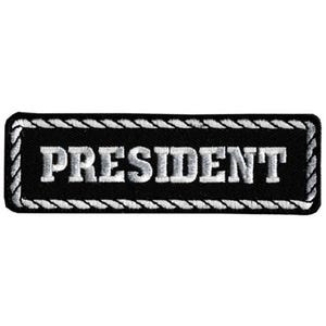 May include: A black rectangular patch with the word "PRESIDENT" embroidered in white block letters. The patch has a white rope-like border.