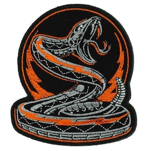 May include: Embroidered patch showing a coiled snake with an open mouth, set against a black background. The snake is detailed with grey and orange stitching, with an orange lightning bolt design. The patch has a black border.