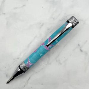Peut inclure: Un stylo à motif tourbillon bleu et rose avec une pointe et un capuchon en métal argenté.