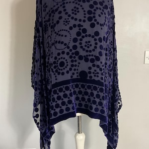 May include: A dark blue, long-sleeved tunic with a velvet polka dot pattern. The tunic has a keyhole neckline and a wide band of velvet at the hem. The fabric is semi-sheer.