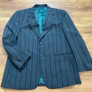 May include: A dark green and navy blue striped blazer with a teal green lining. The blazer has a two-button closure, a notched lapel, and three buttons on each cuff. The jacket is laid flat on a wooden surface.